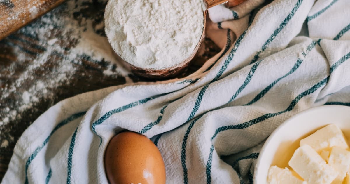 A wooden measuring cup full of flour with an egg and butter nearby