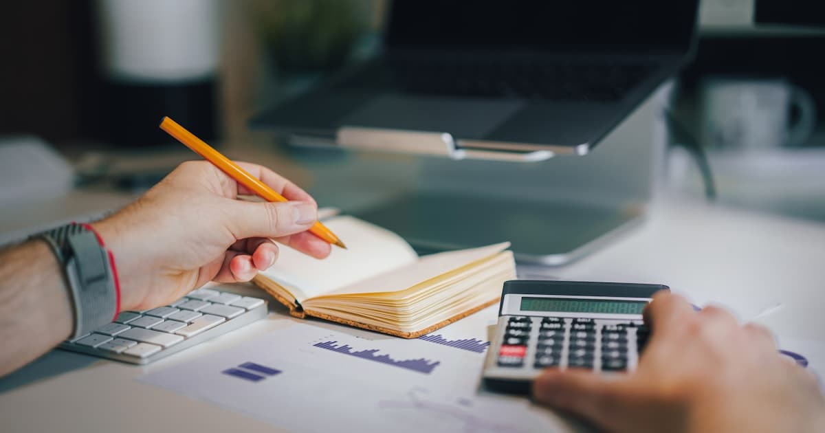 A person using a calculator beside a notebook and printed charts